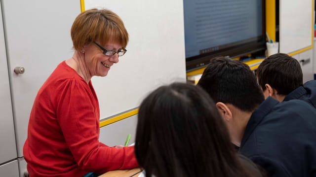 A teacher supports pupils working at computers in a classroom.