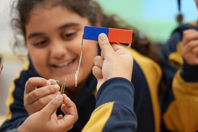 A pupil holds a small blue and red object during a classroom activity.