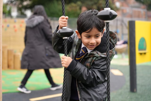 A pupil smiles while holding the rope of an outdoor playground swing.