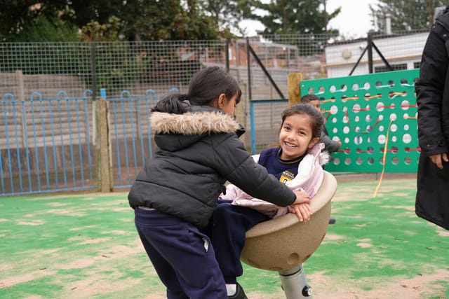 Two pupils spin together on playground equipment.