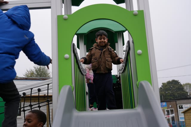 A pupil stands inside a green playground playhouse.