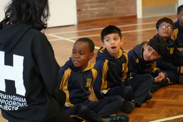 Pupils sit in the school hall during a PE lesson.
