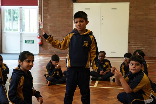 A pupil holds up an object while classmates sit in a circle during PE.