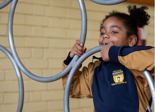 A pupil smiles while climbing on outdoor play equipment.