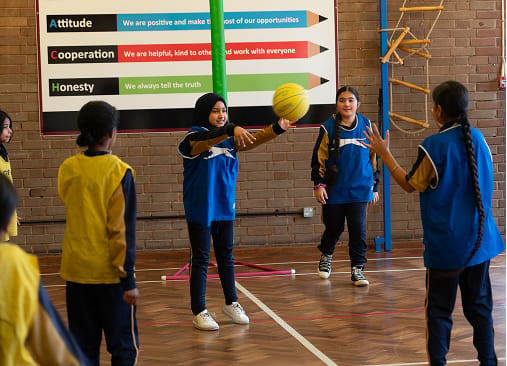 Pupils play basketball in the school sports hall, with one pupil passing the ball.