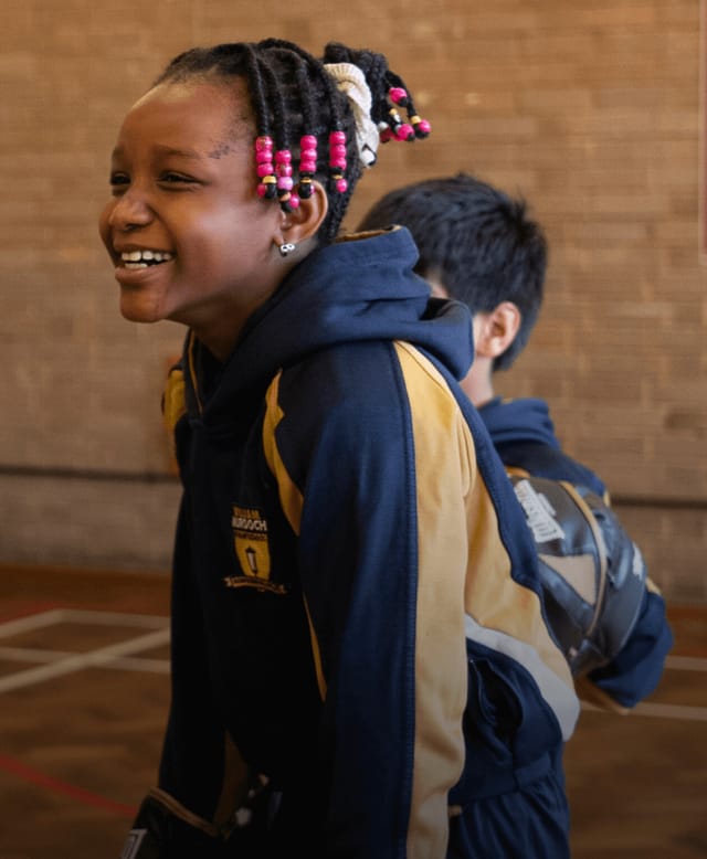 A pupil smiles during a PE activity in the school hall.