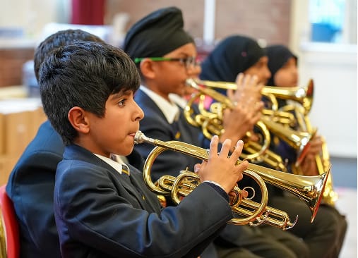 Pupils in school uniform play brass instruments during a music lesson.
